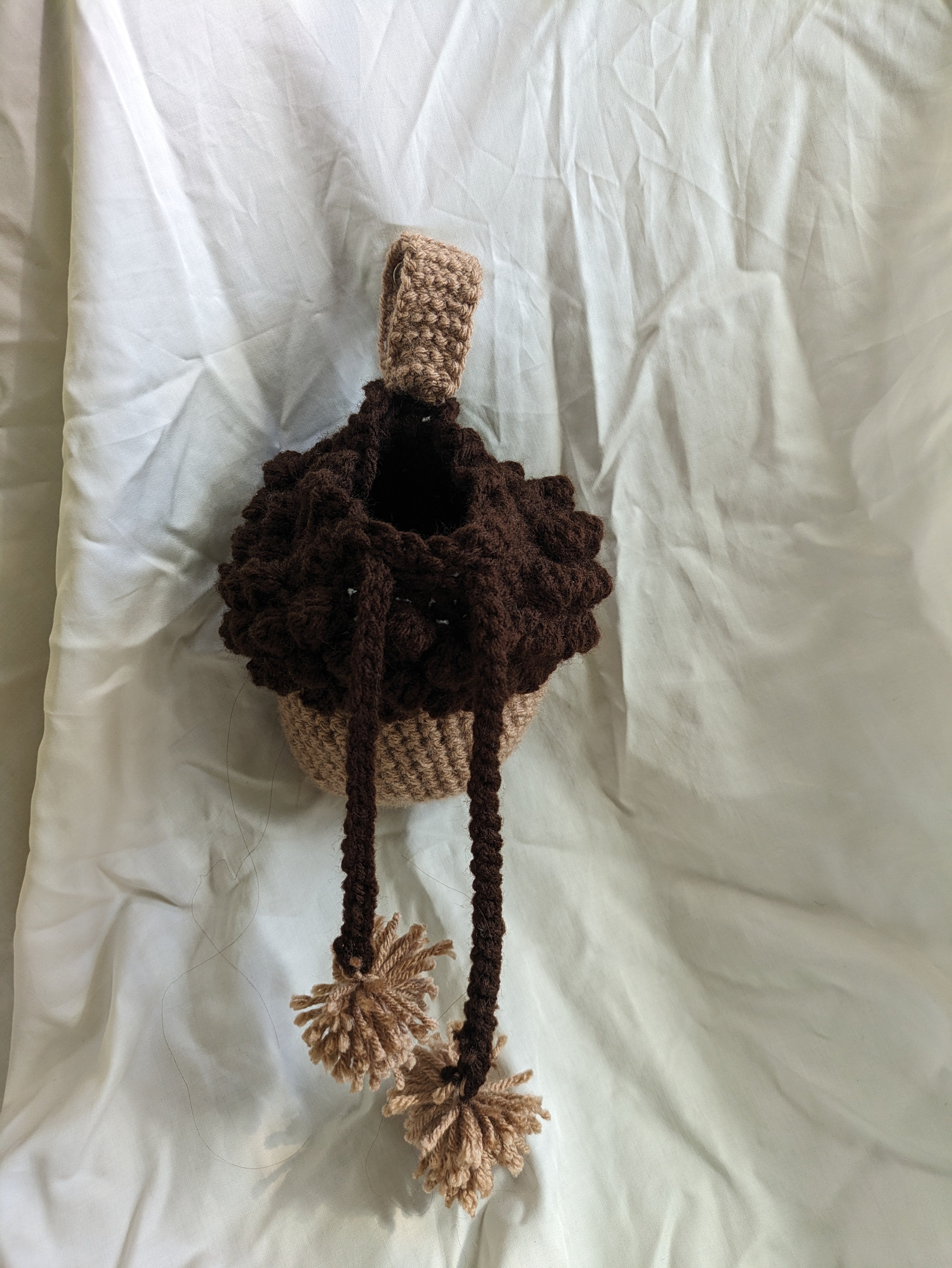 Crocheted acorn bag with pom-poms on a white surface, opened to show inside of bag.