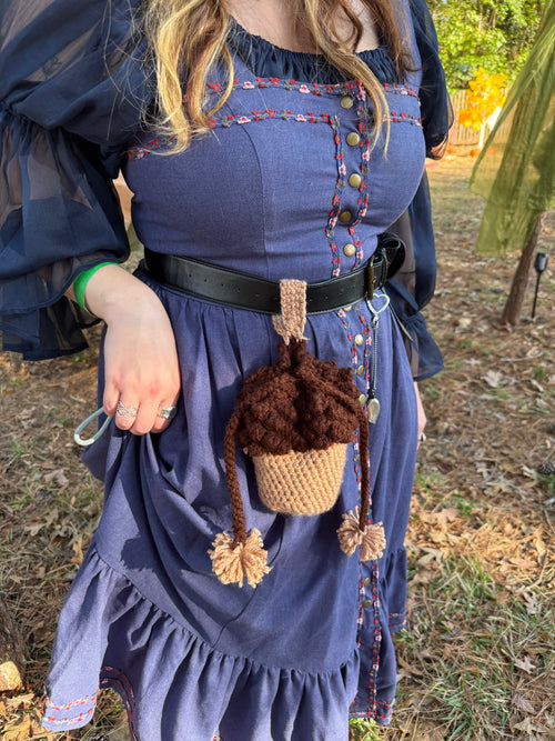 Person wearing a blue dress with decorative buttons, holding a brown acorn-shaped bag.