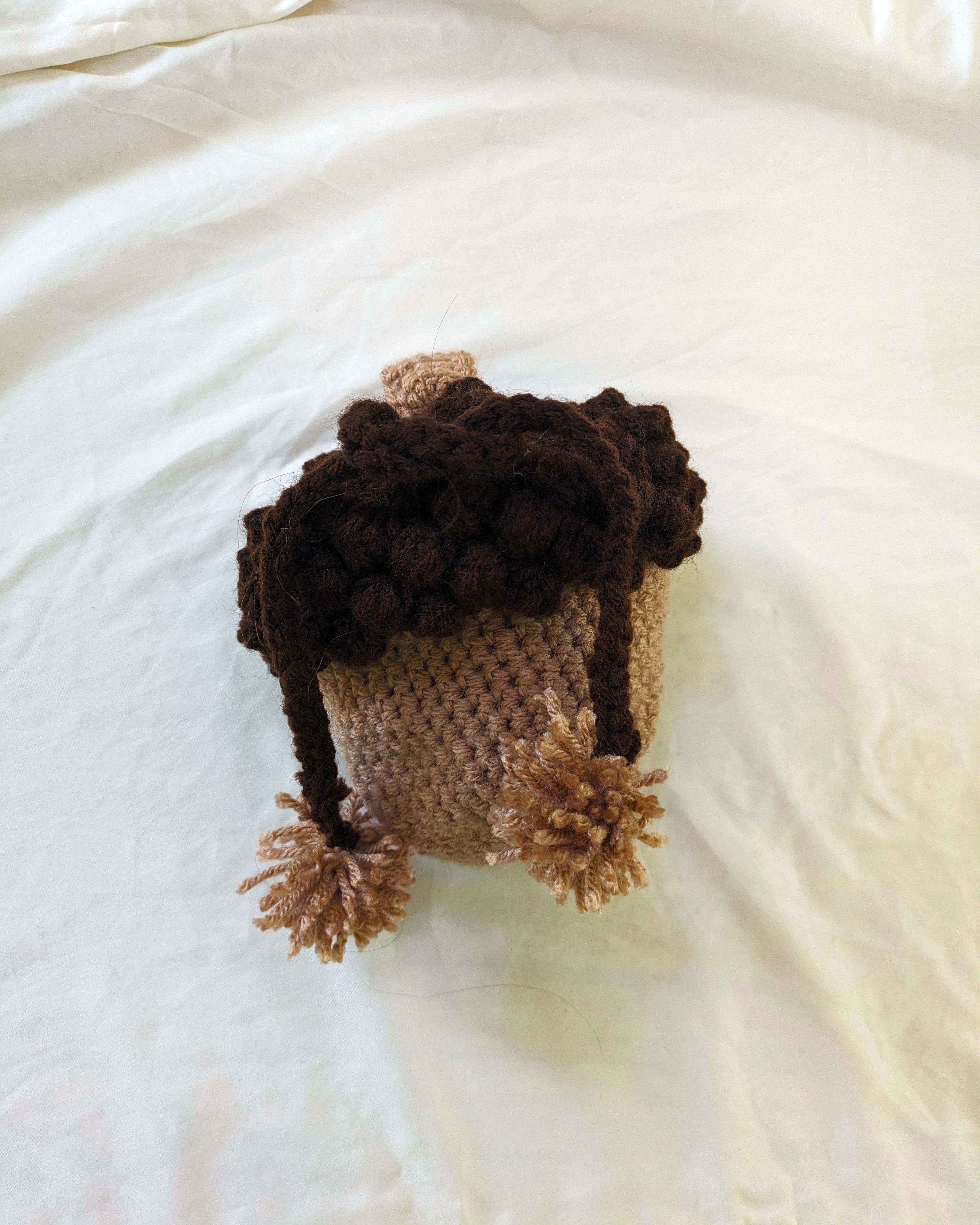 Crocheted acorn bag with pom-poms on a white surface