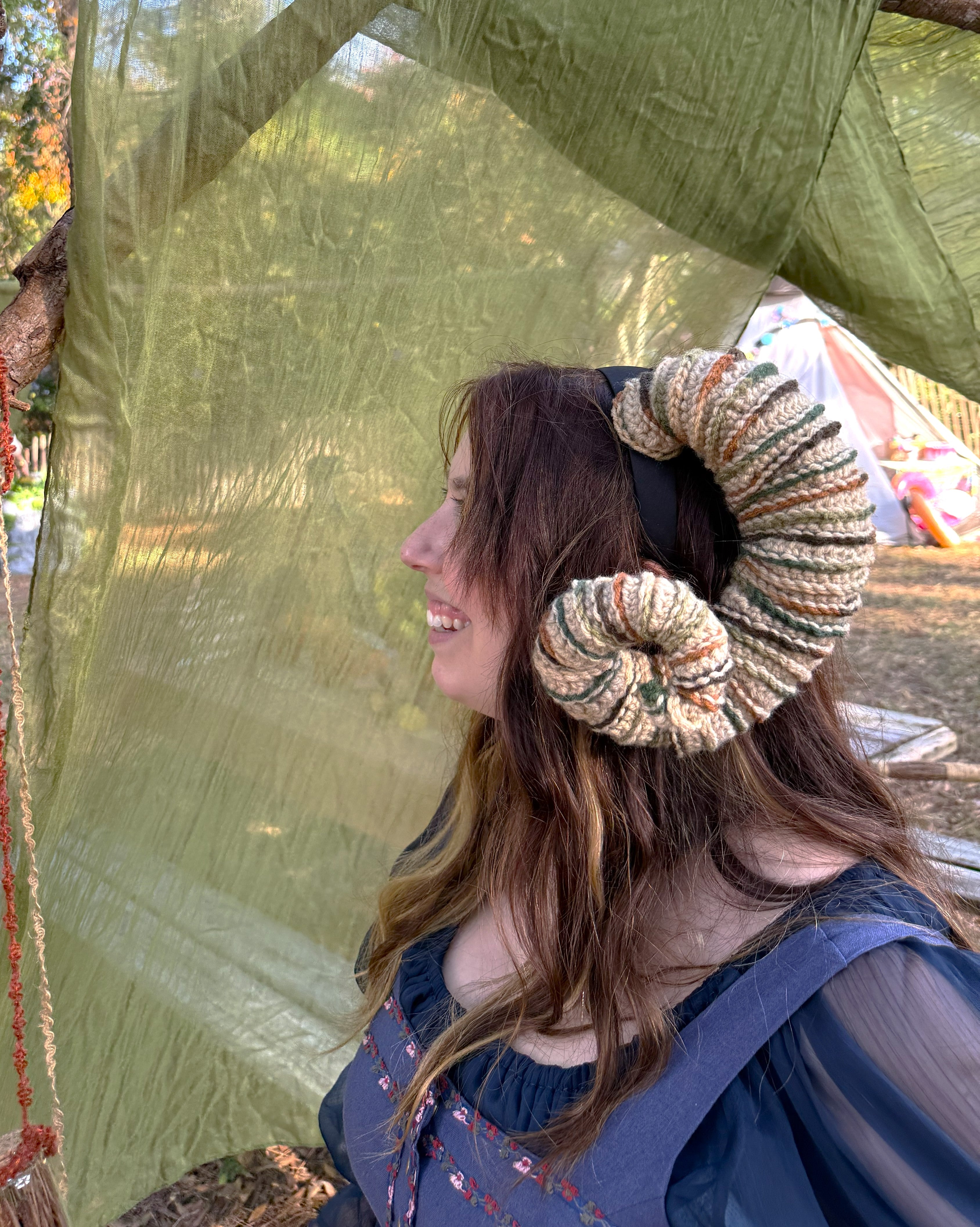 Person wearing large, decorative ram horns in front of a green fabric backdrop