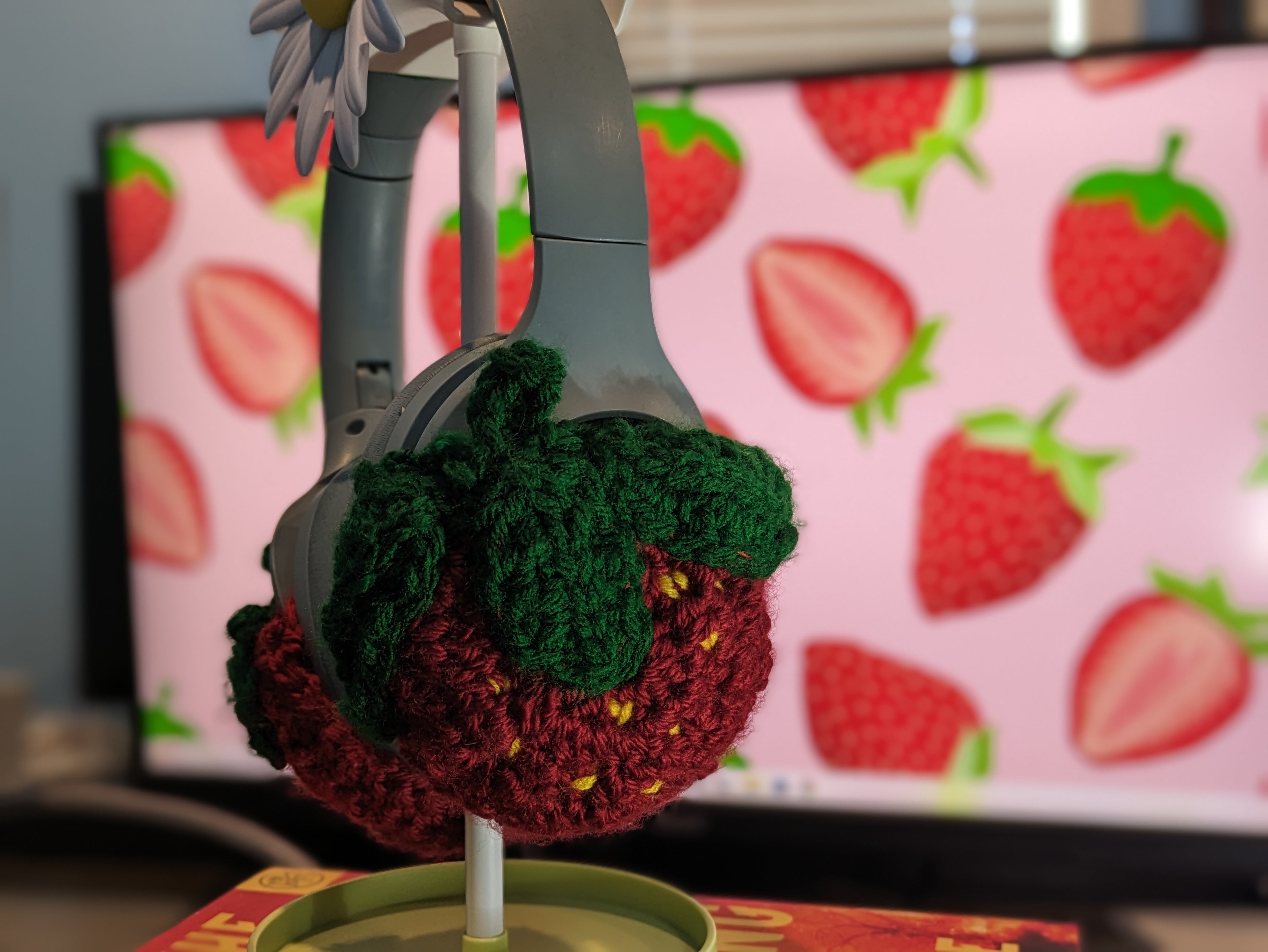 Crocheted strawberry decoration on a pair of headphones with a strawberry-patterned background.