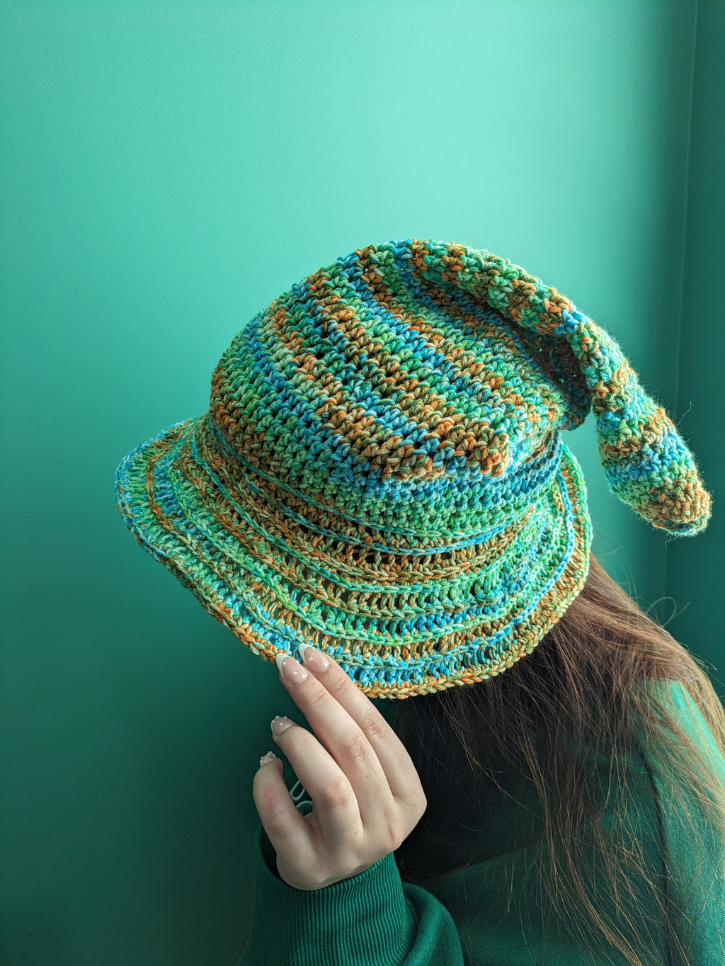 Crocheted hat with blue and orange pattern held by a person against a teal background
